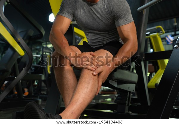 A man injuredand painful from an accident. Leg\
pain. Muscle strength training workout at gym fitness center club.\
Exercise indoor with sport equipment. Athletic. People lifestyle.\
Hurt or cramps.
