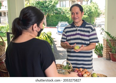 A man inquires about the price of a green mango to a vendor at a small vegetable stall at a village weekend market.