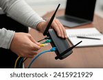 Man inserting cable into Wi-Fi router at wooden table indoors, closeup