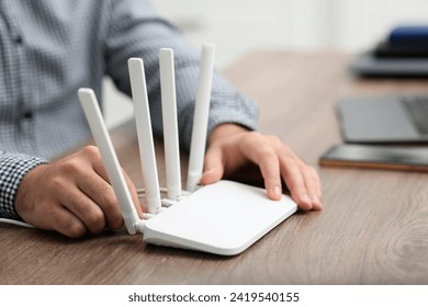 Man inserting cable into Wi-Fi router at wooden table indoors, closeup