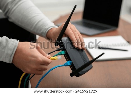 Man inserting cable into Wi-Fi router at wooden table indoors, closeup