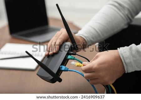 Man inserting cable into Wi-Fi router at wooden table indoors, closeup