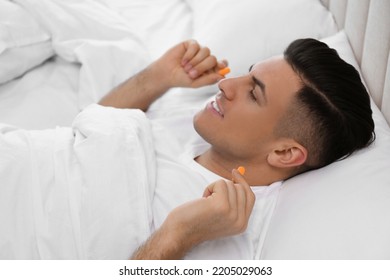 Man Inserting Foam Ear Plugs In Bed