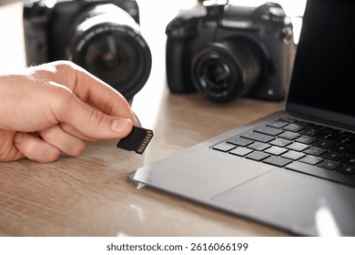 Man inserting SD memory card into laptop at wooden table indoors, closeup