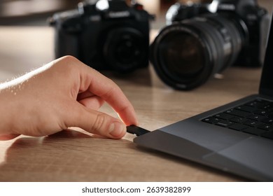Man inserting SD memory card into laptop at wooden table indoors, closeup