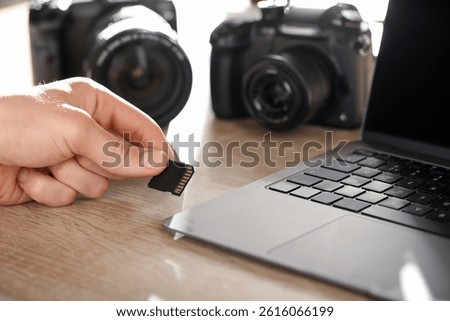 Man inserting SD memory card into laptop at wooden table indoors, closeup