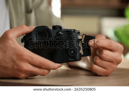 Man inserting SD memory card into photo camera at wooden table indoors, closeup