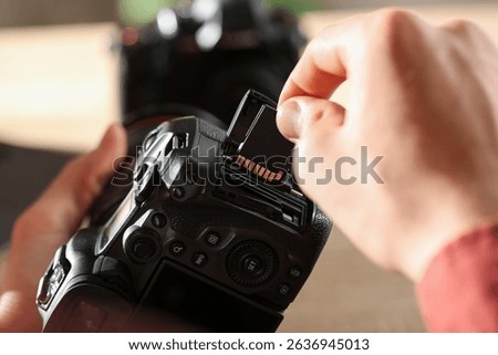 Man inserting SD memory card into photo camera indoors, closeup