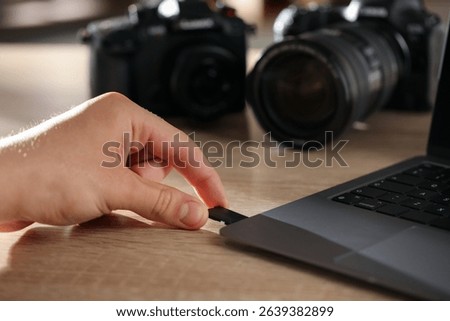 Man inserting SD memory card into laptop at wooden table indoors, closeup