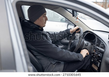 A man inside a car, the driver behind the wheel in cold weather