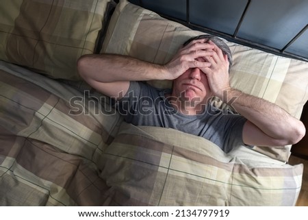 Man with insomnia lying in bed and snorting from exhaustion.