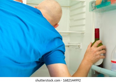 A Man Inspecting An Empty Fridge Holding A Wine Bottle, Focus In The Foreground