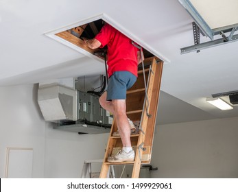 Man Inspecting Garage Attic. Male Homeowner Climbing Wooden Pull Down Attic Ladder.