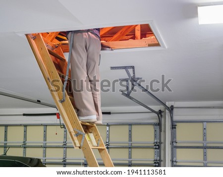 Man inspecting garage attic. Male homeowner climbing wooden pull down attic ladder stairs.