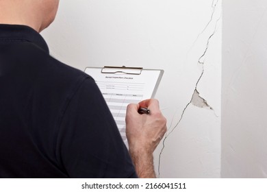 Man with inspection checklist in front of a white wall with a long crack or rip and a piece of plaster missing, rental damage concept. - Shutterstock ID 2166041511