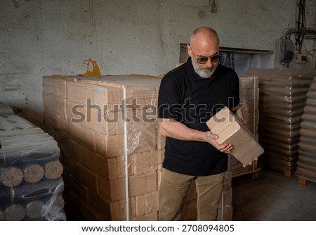 A man inspects a batch of packaged NESTRO briets in a warehouse. Stacks of goods are visible in the background, indicating the warehouse's busy schedule.