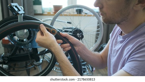 Man Inspects Bicycle Inner Tube For Punctures. Trying On A Tire. Looks At The Sealed Patches. The Concept Of A Home Bike Workshop, Do It Yourself, Repair It. Close-up, Indoors.