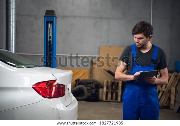 Man\
inspects a car and uses a tablet. Medium\
shot