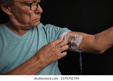 A man inspects the PICC line inserted in his upper arm