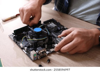 Man installing computer chip onto motherboard at wooden table, closeup