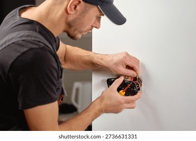 Man installing electrical wall switch and connecting wires inside white wall using screwdriver. Concept of electrician work, home renovation, electrical installation and maintenance.