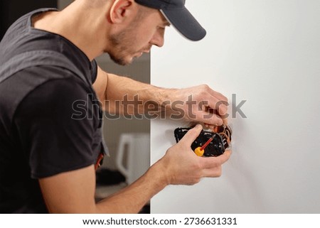 Man installing electrical wall switch and connecting wires inside white wall using screwdriver. Concept of electrician work, home renovation, electrical installation and maintenance.