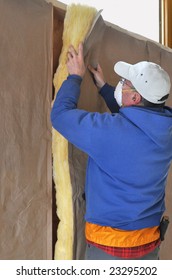 Man Installing Fiberglass Insulation To Wall Cavity