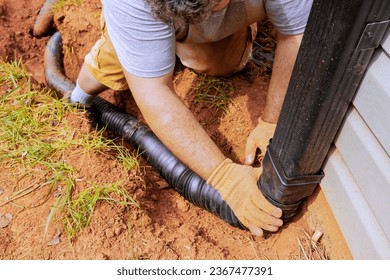 Man installing flexible gutter extension drainage pipe connector downspout with water draining down