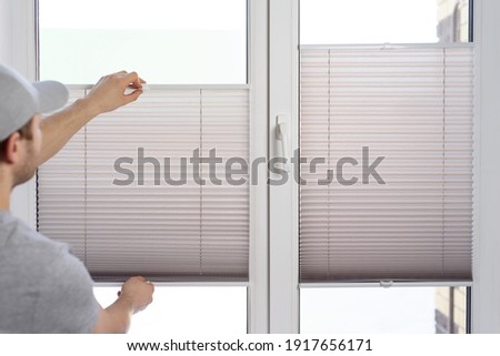 Man installing gray pleated blinds on the window
