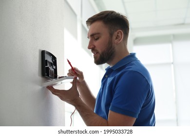 Man Installing Home Security System On White Wall In Room