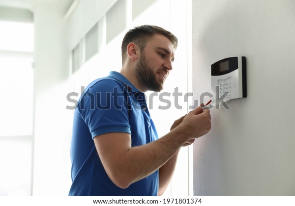 Man\
installing home security system on white wall in\
room