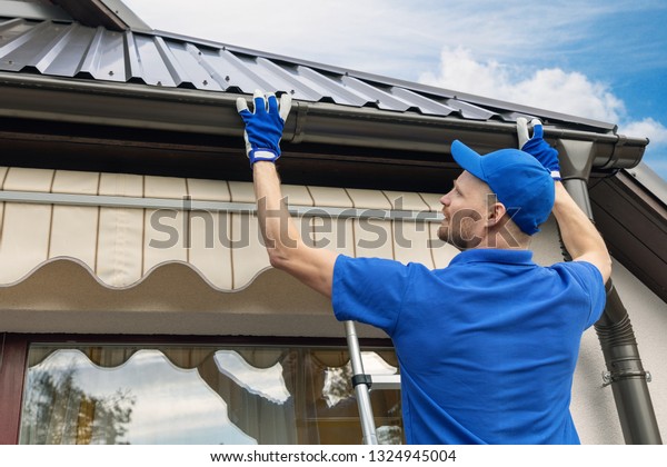 man installing\
house roof rain gutter\
system