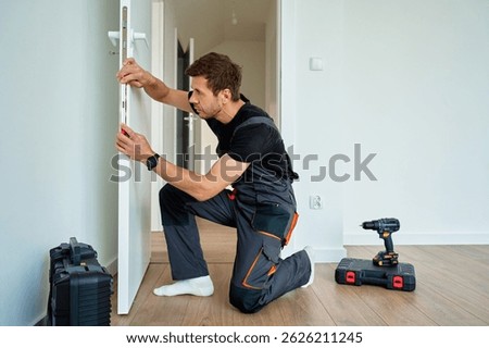 Man installing interior door using spirit level. Professional craftsman in uniform aligning door with tools during home renovation