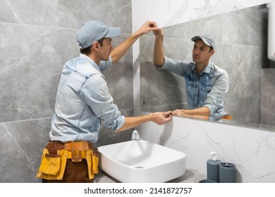 Man installing a mirror on wall in his renewed bathroom - Shutterstock ID 2141872757