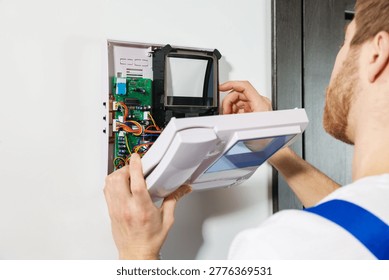 Man installing modern intercom system on white wall indoors, closeup