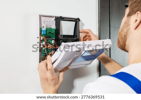 Man installing modern intercom system on white wall indoors, closeup