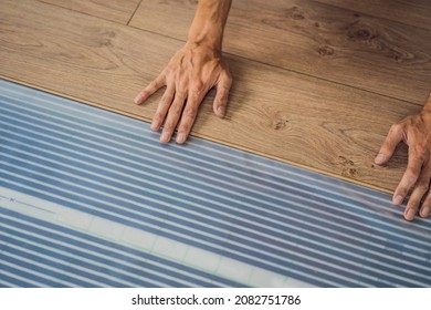 Man Installing New Wooden Laminate Flooring On A Warm Film Floor. Infrared Floor Heating System Under Laminate Floor