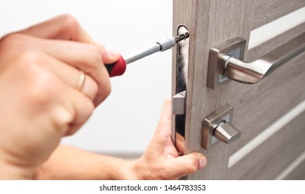 The man is installing the part of the wooden door by the screwdriver