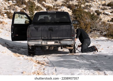 Man Installing And Putting On Chains On His Truck Tires To Drive Uphill On An Unpaved Dirt Road In The Winter Snow Weather For Safety To Avoid Getting Stuck In A Snowbank