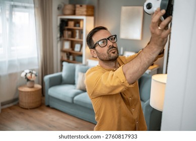 Man installing a security camera on a wall, ensuring home safety and utilizing smart technology for protection and continuous surveillance in a modern living room setting