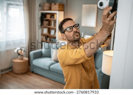 Man installing a security camera on a wall, ensuring home safety and utilizing smart technology for protection and continuous surveillance in a modern living room setting