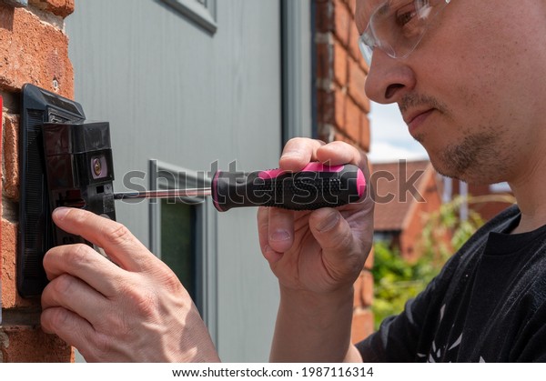 Man installing a\
smart doorbell with security camera and solar charger next to the\
front door of his house