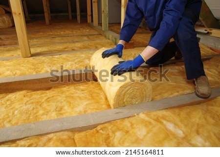 Man installing thermal insulation layer under the roof, using mineral glass wool 