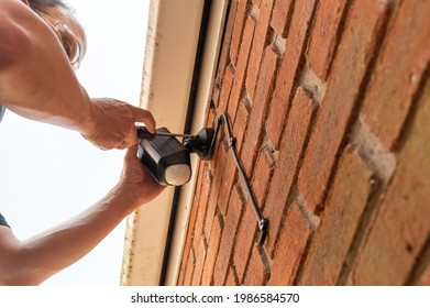 Man installing a wireless security camera and floodlight onto the outside of a garage 