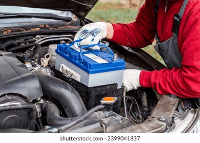 A man installs a car battery under the hood of a car. Vehicle maintenance and repair. - Powered by Shutterstock