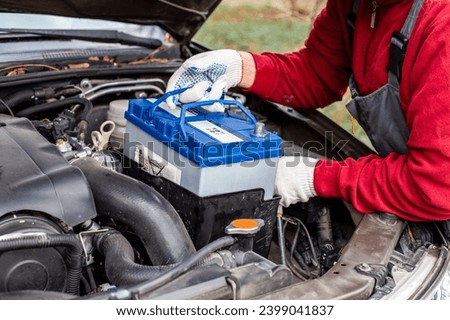 A man installs a car battery under the hood of a car. Vehicle maintenance and repair.