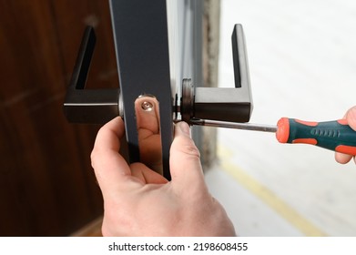 A man installs a door handle in a door, carpentry work at home, repair and restoration work. - Shutterstock ID 2198608455