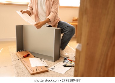 Man with instructions assembling chest of drawers at home
