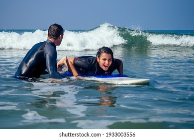 man instructor demonstrating how to paddle in the water by hands on surfboard to indian woman in surf class in Goa sea - Powered by Shutterstock