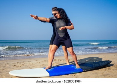 man instructor demonstrating how to stand up on surfboard to indian woman in surf class in Goa sea - Powered by Shutterstock - Get 15% off with code: PIKWIZARD15